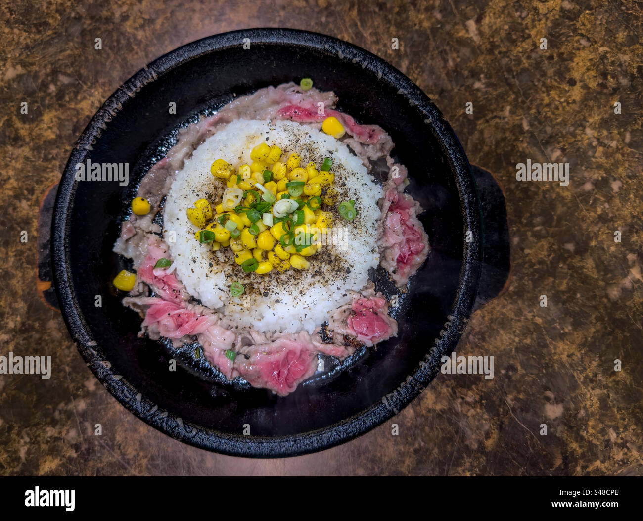 Serving of beef with peppered rice and corn on sizzling stone plate ...