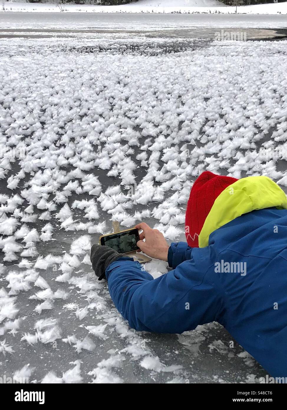 A man lies on the ice and photographs snow crystals. - Smartphone Captured Stock Image