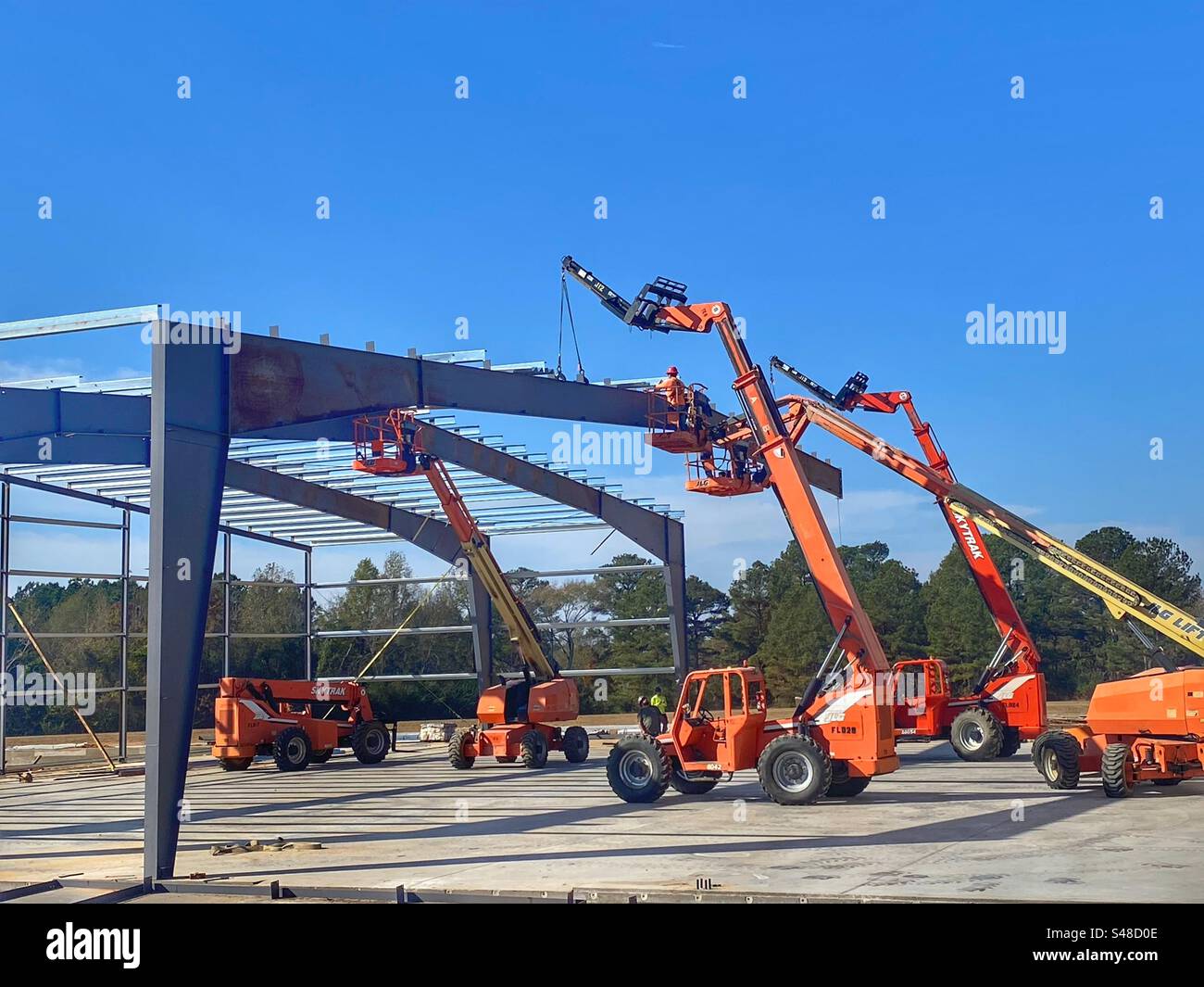 Construction workers building a steel machine shed with several cherry pickers - Smartphone Captured Stock Image