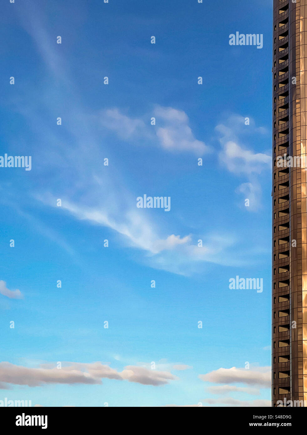 Low angle view of skyscraper on blue sky with a few swirling white clouds on a sunny afternoon with copy space. Abstract. Tranquility. Modern. - Smartphone Captured Stock Image