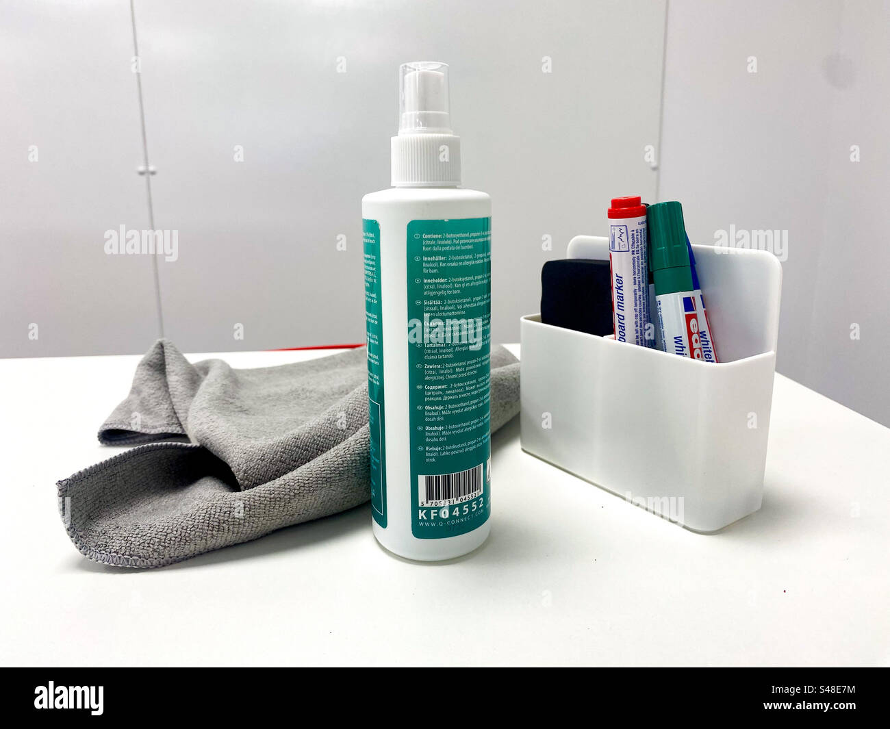 Whiteboard markers, bottle of cleaning fluid and cleaning cloth on a white table with a
