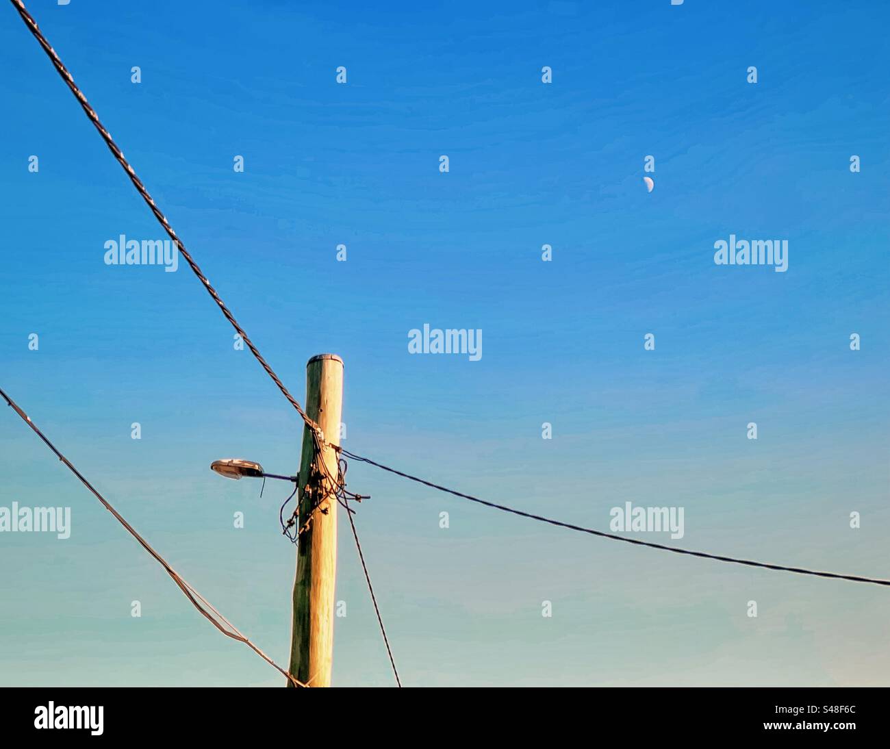 Low angle view of electricity pylon and cables on blue sky with sickle moon in the morning. Technology. Nature. - Smartphone Captured Stock Image