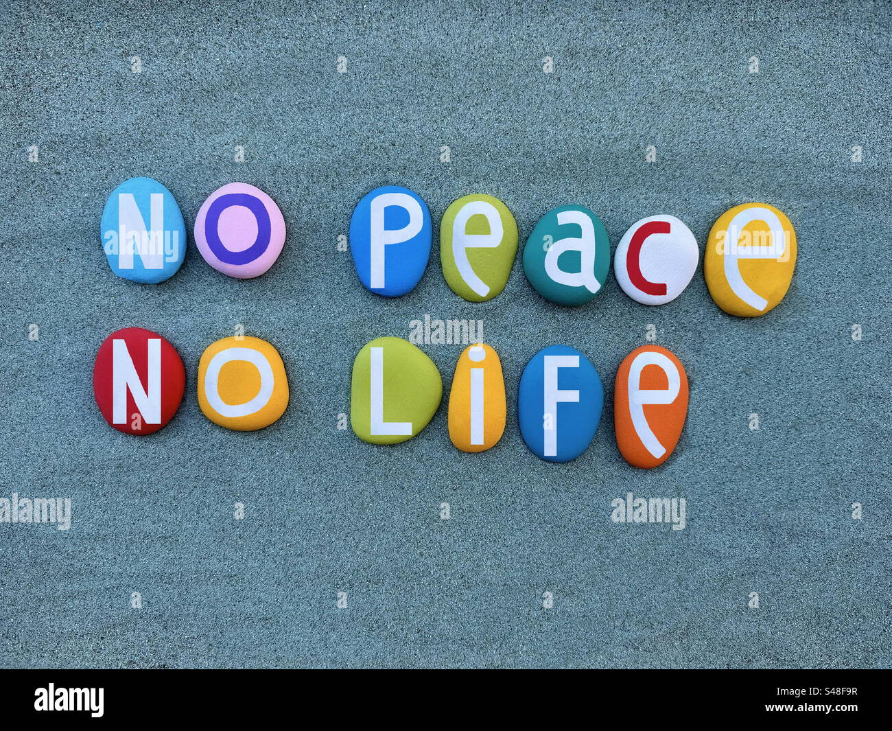 No peace, no life, creative slogan composed with hand painted multi colored stone letters over green sand - Smartphone Captured Stock Image