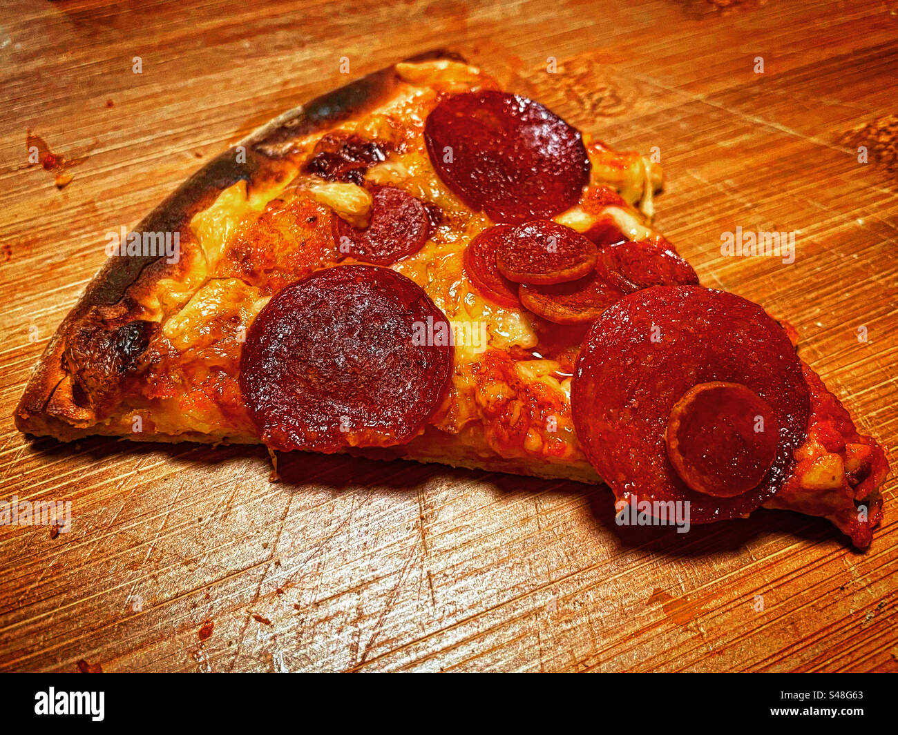 photo visual of a single triangle slice piece of pizza with cheese and pepperoni just baked on a wood plate - Smartphone Captured Stock Image