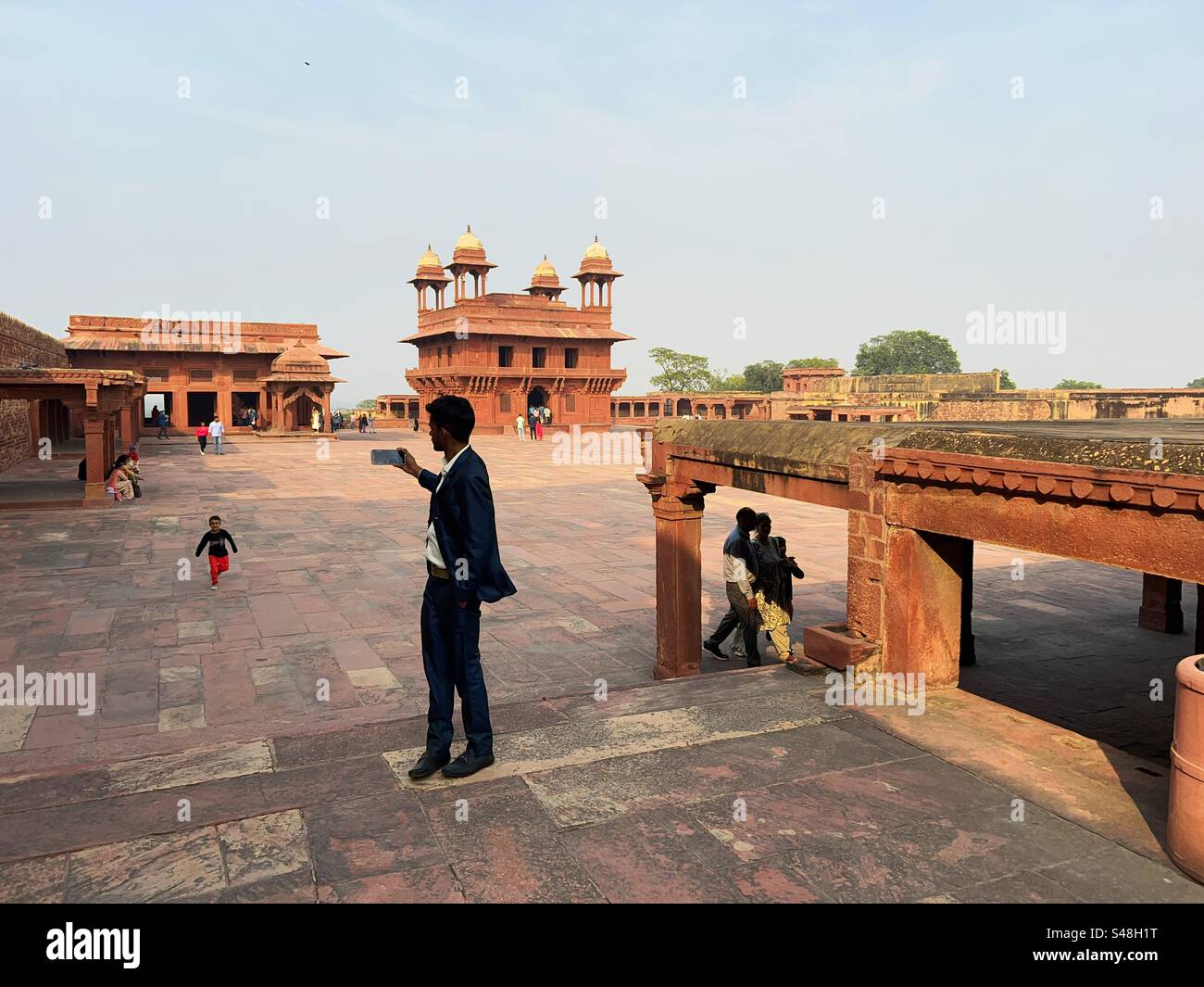 An Indian man dressed in a suit clicking pictures of Akbar’s palace in UNESCO World Heritage Site, Fatehpur Sikri in India - Smartphone Captured Stock Image