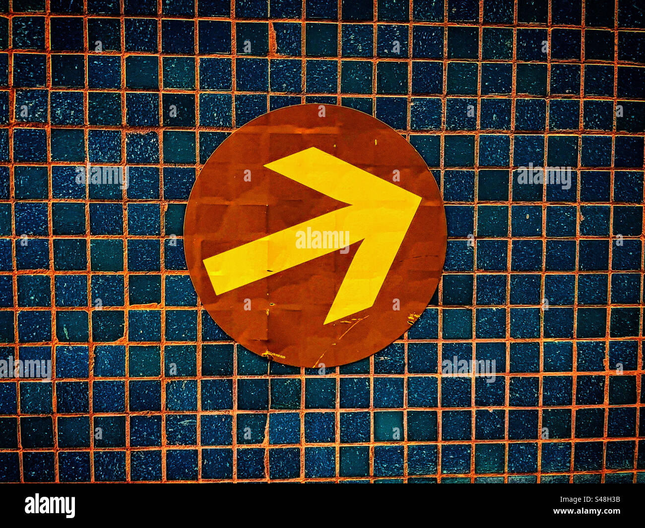 yellow arrow in a brown circle is pointing up right direction against a tiled wall - Smartphone Captured Stock Image