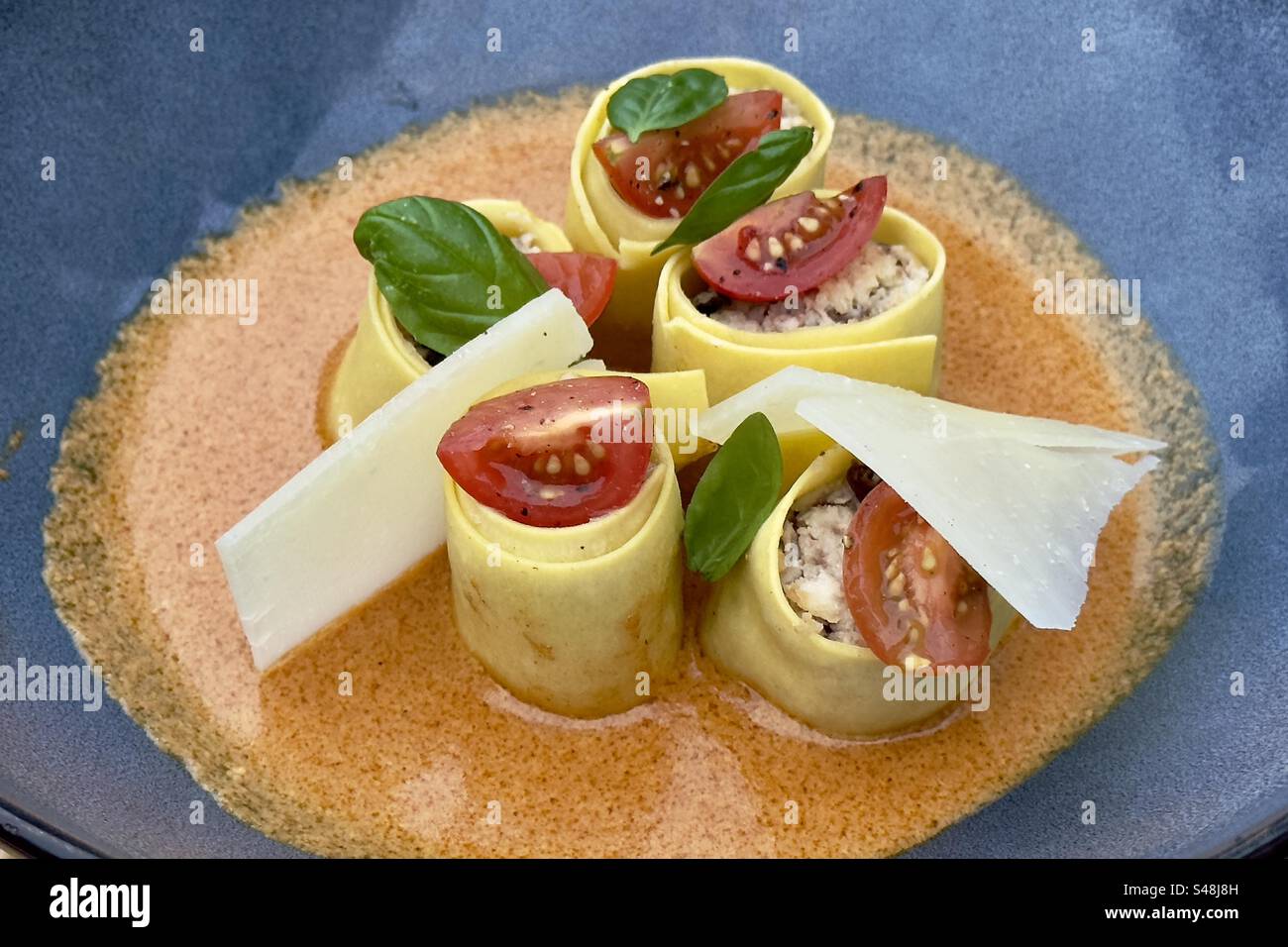 Close-up shot of a colourful plate of lasagna pasta on a restaurant plate in France, with tomatoes, basil, sauce and sliced cheese - Smartphone Captured Stock Image
