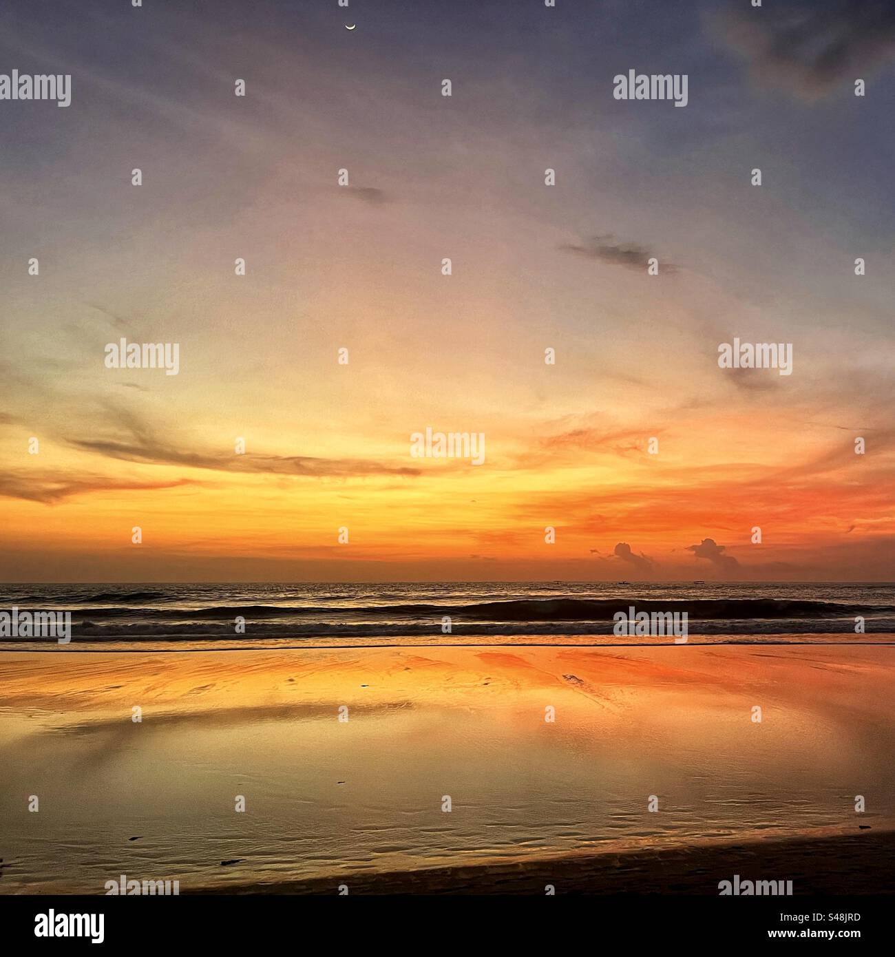 Sunset at Seminyak beach Bali with the sun set over the sea and the orange glow remaining in the clouds and the orange light reflecting in the shallow water - Smartphone Captured Stock Image