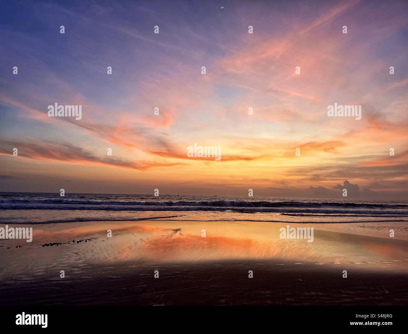 Sunset at Seminyak beach Bali with the sun set over the sea and the orange glow remaining in the clouds and the orange light reflecting in the shallow water - Smartphone Captured Stock Image