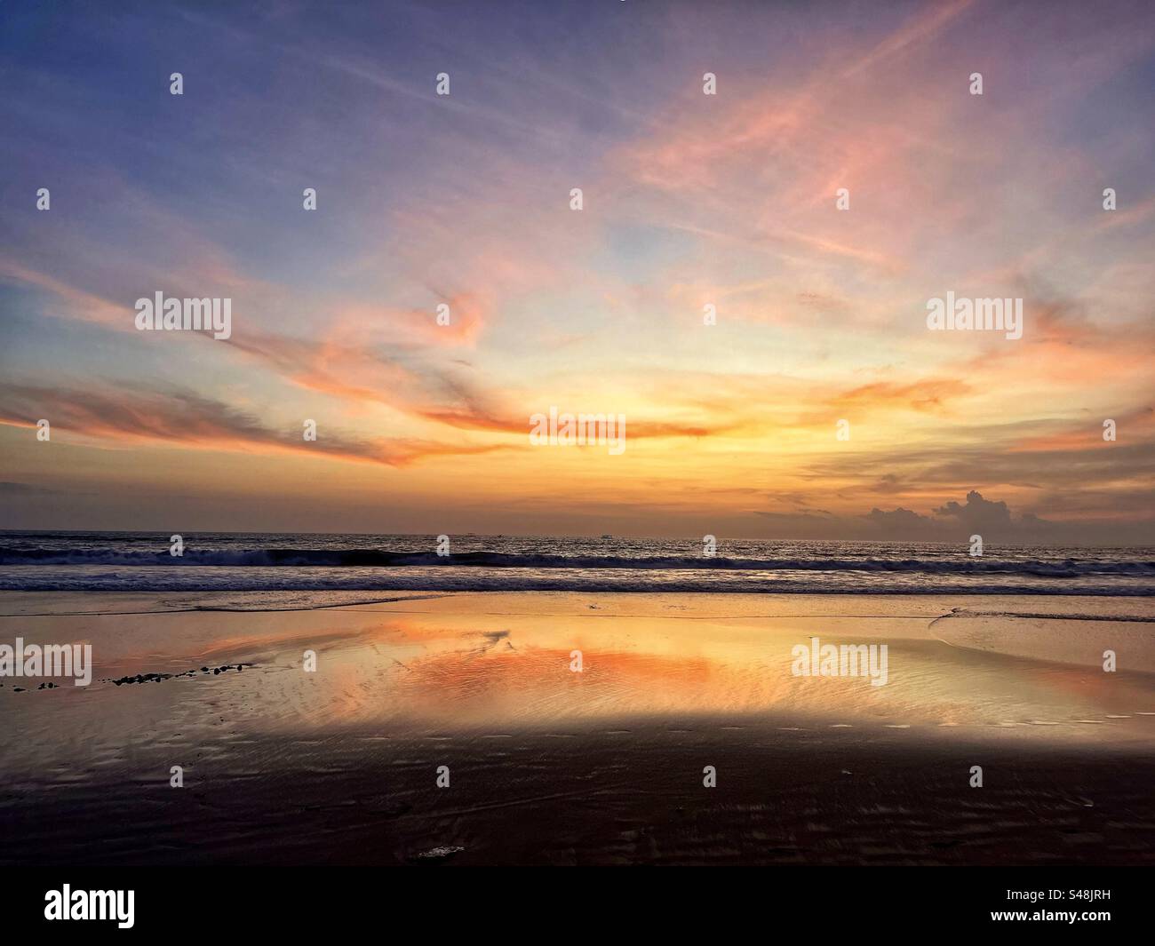 Sunset at Seminyak beach Bali with the sun set over the sea and the orange glow remaining in the clouds and the orange light reflecting in the shallow water - Smartphone Captured Stock Image