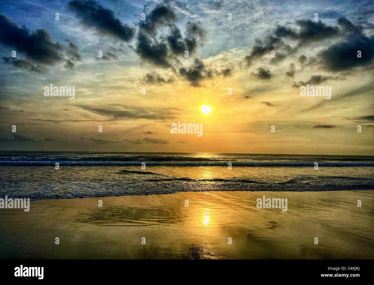 Sunset at Seminyak beach Bali with the sun set over the sea and the orange glow remaining in the clouds and the orange light reflecting in the shallow water - Smartphone Captured Stock Image