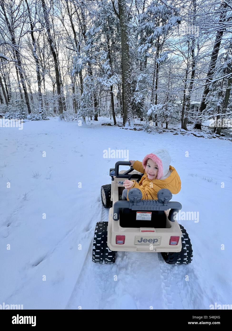 Toddler driving a jeep power wheel in the snow Stock Photo