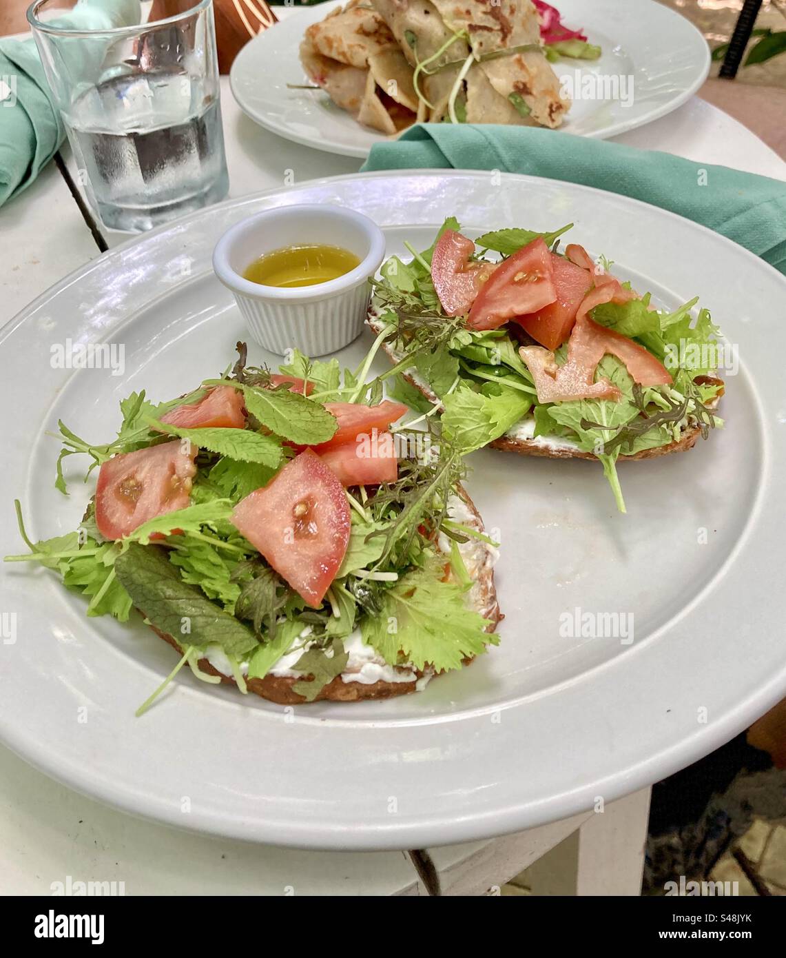 Multigrain bread covered in soft goat cheese, leafy greens and tomatoes with a side of olive oil. Stock Photo