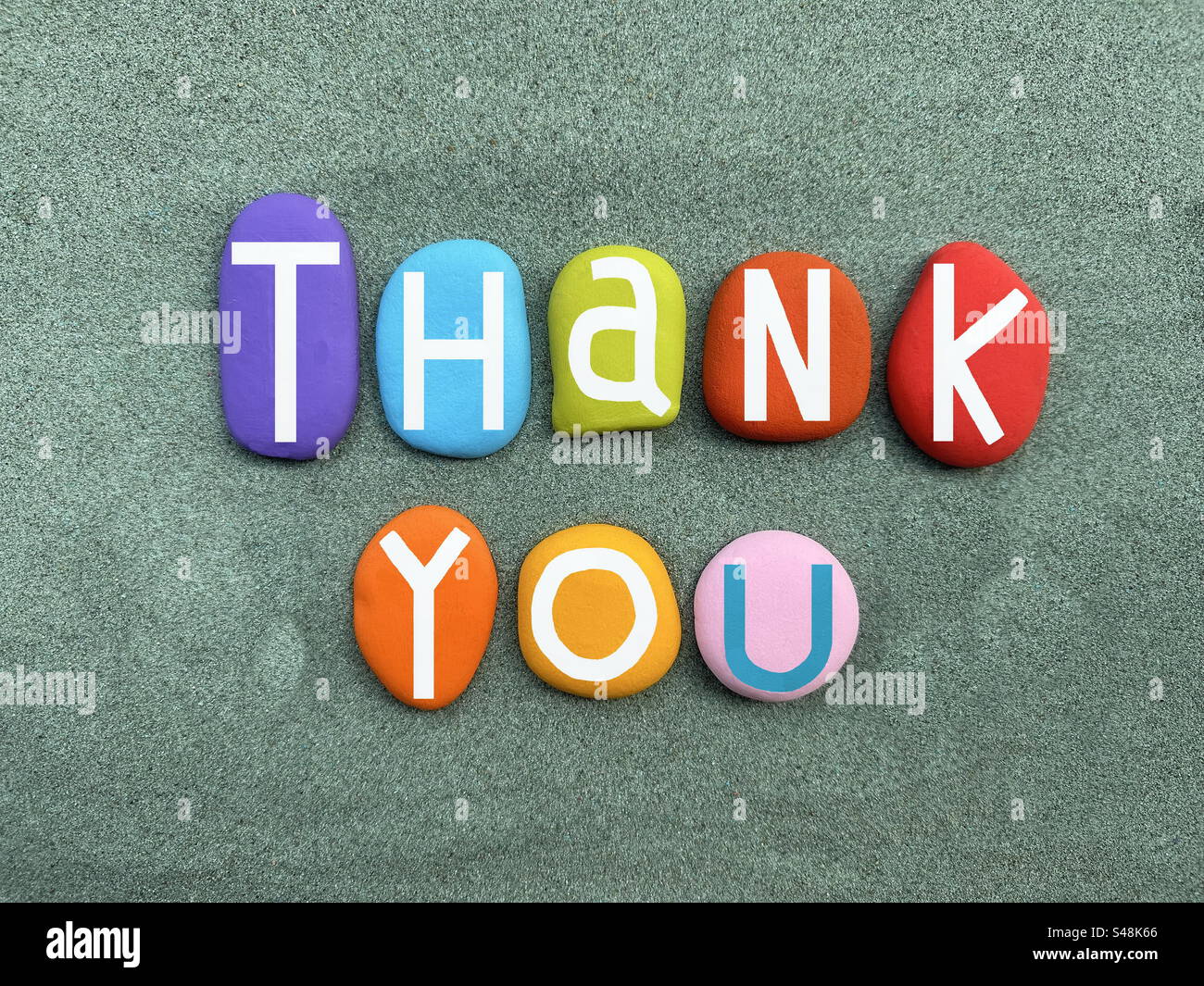 Thank you, creative text composed with multi colored stone letters over green sand - Smartphone Captured Stock Image