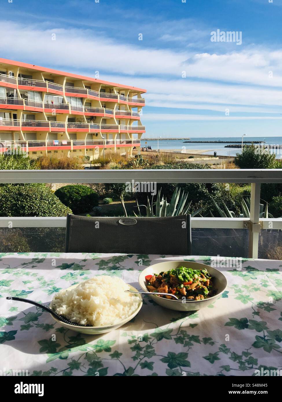 Portrait shot of two dishes on a flowery table top on a balcony with view of the Mediterranean - Smartphone Captured Stock Image