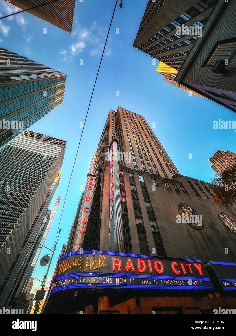 Looking up at Radio City Music Hall building and surrounding skyscrapers against vivid blue sky - Smartphone Captured Stock Image