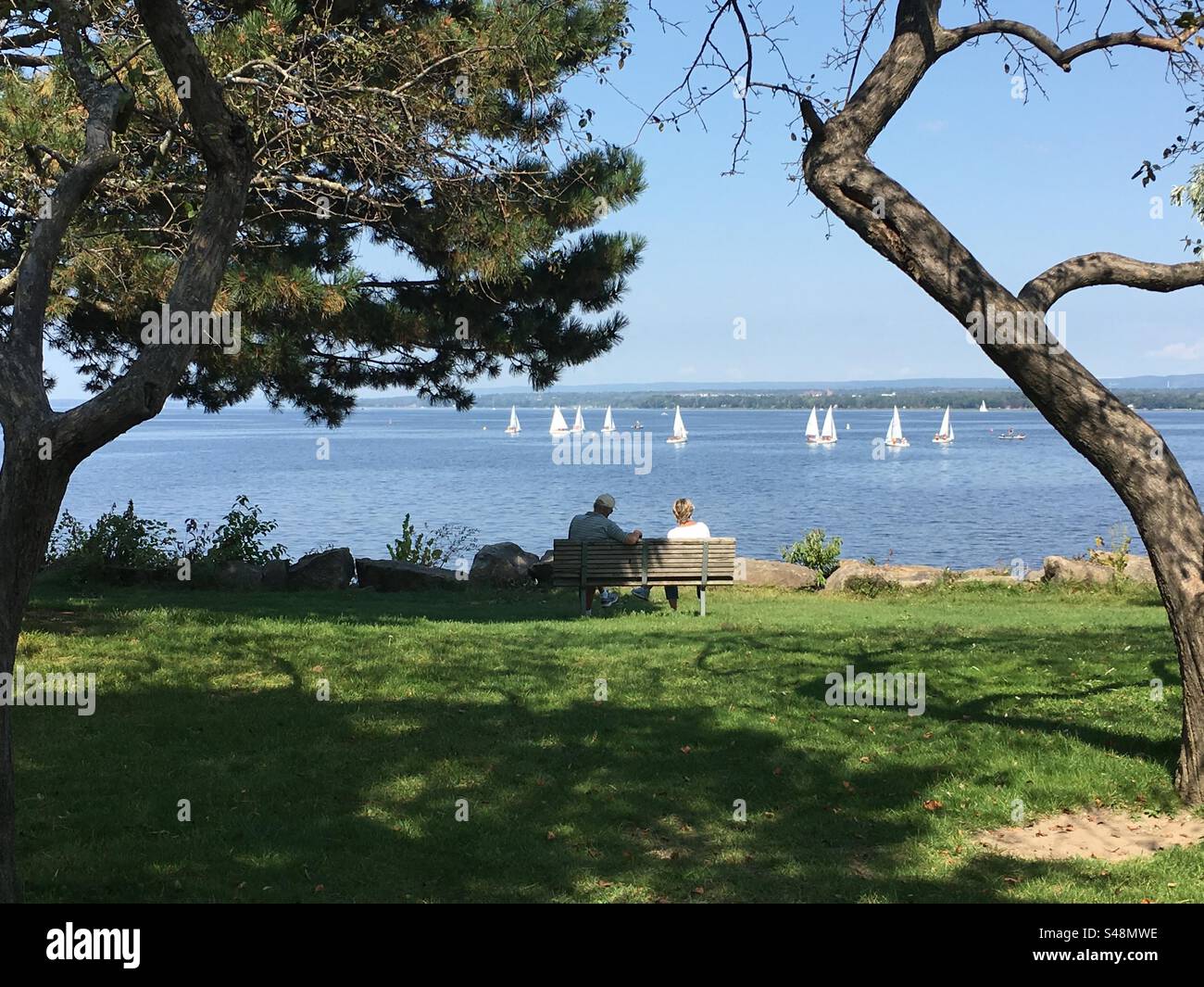 Beautiful picturesque landscape photo of a couple sitting on a park bench facing the river in Ottawa, Ontario, Canada - Smartphone Captured Stock Image