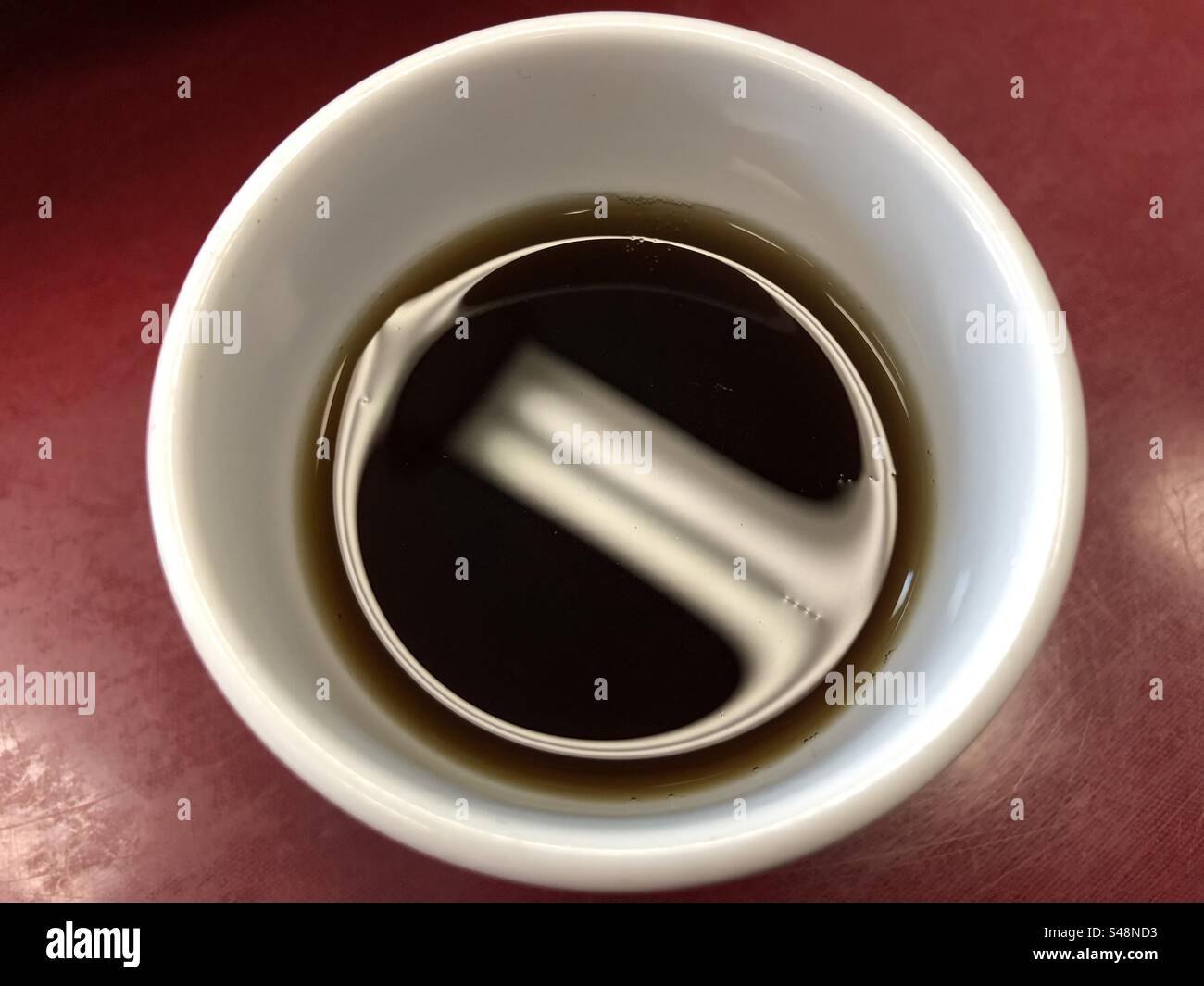 Top-down close-up shot of a cup of coffee, ceiling light reflecting off the liquid - Smartphone Captured Stock Image