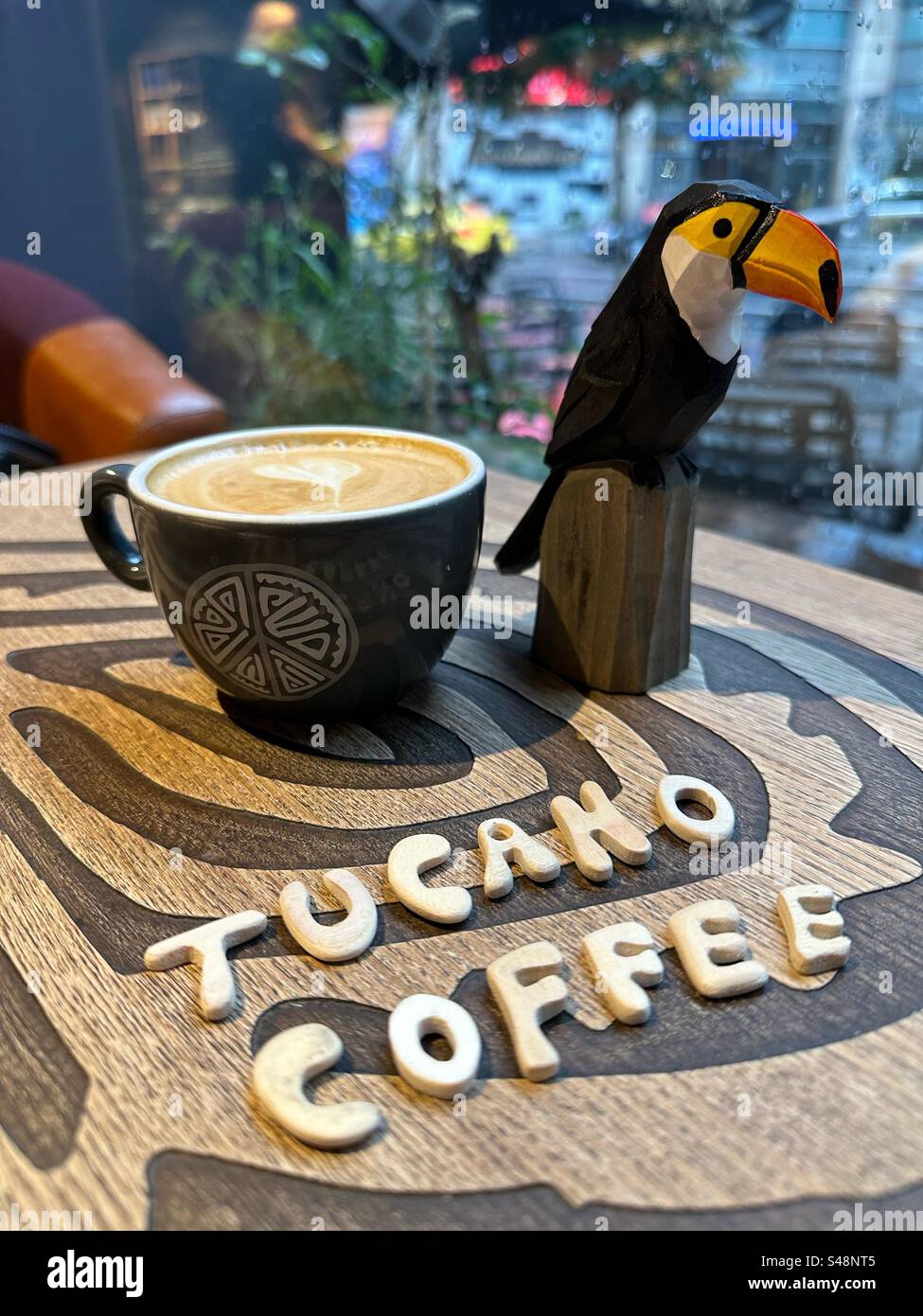 Tucano coffee, creative breakfast in Bucharest with a wooden tucano miniature, a cappuccino and wooden letters - Smartphone Captured Stock Image