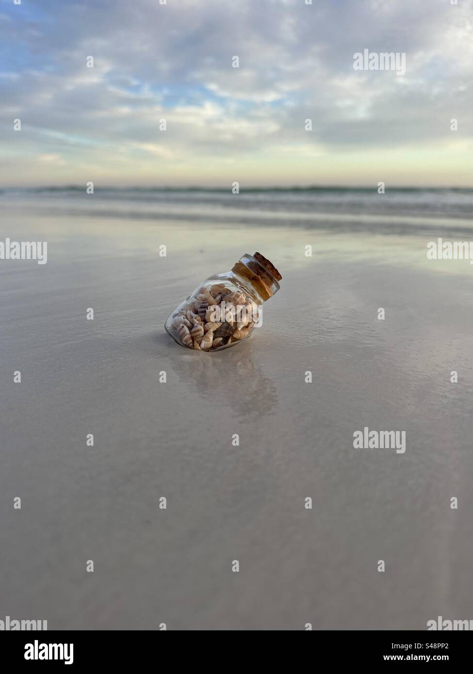 Small bottle with tiny seashells on beach sand - Smartphone Captured Stock Image