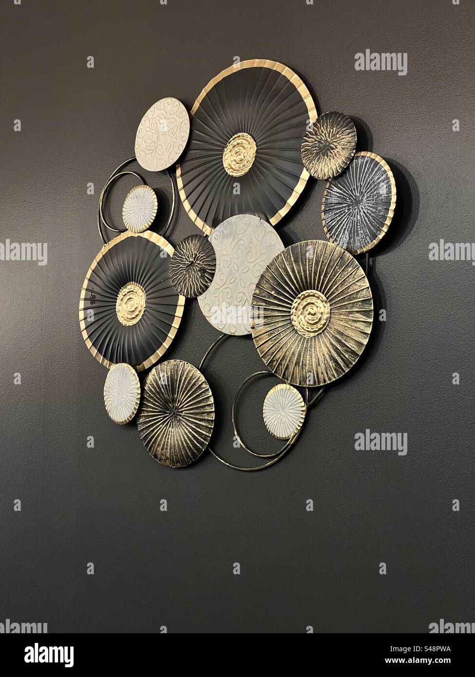 A golden, silver and black wall ornament on a black wall - Smartphone Captured Stock Image