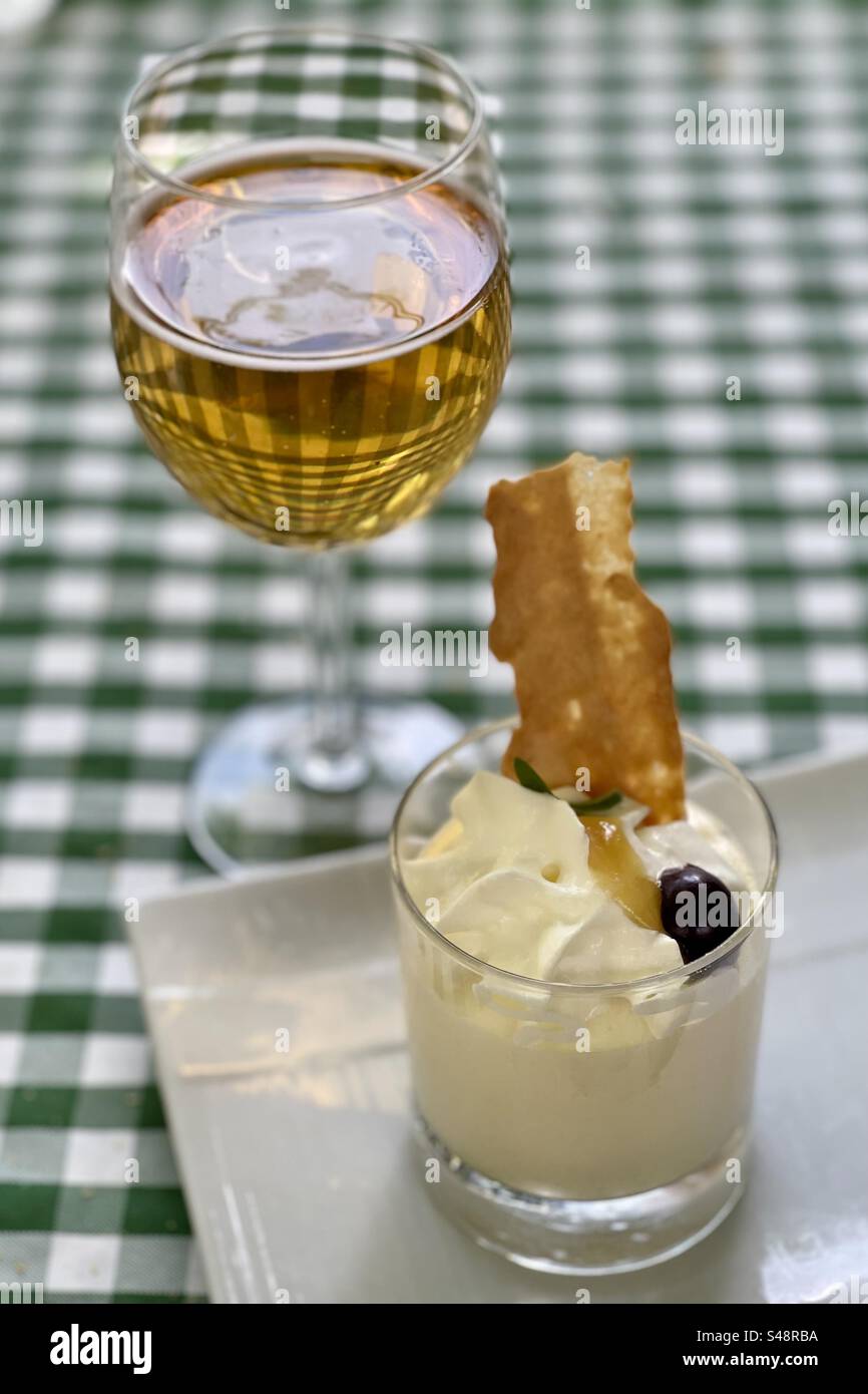Shot of a creamy dessert dish in a glass, with a cherry and a cookie, and a glass of white wine or beer in the background, on a checkered tablecloth in a French restaurant in Montpellier, Occitanie - Smartphone Captured Stock Image
