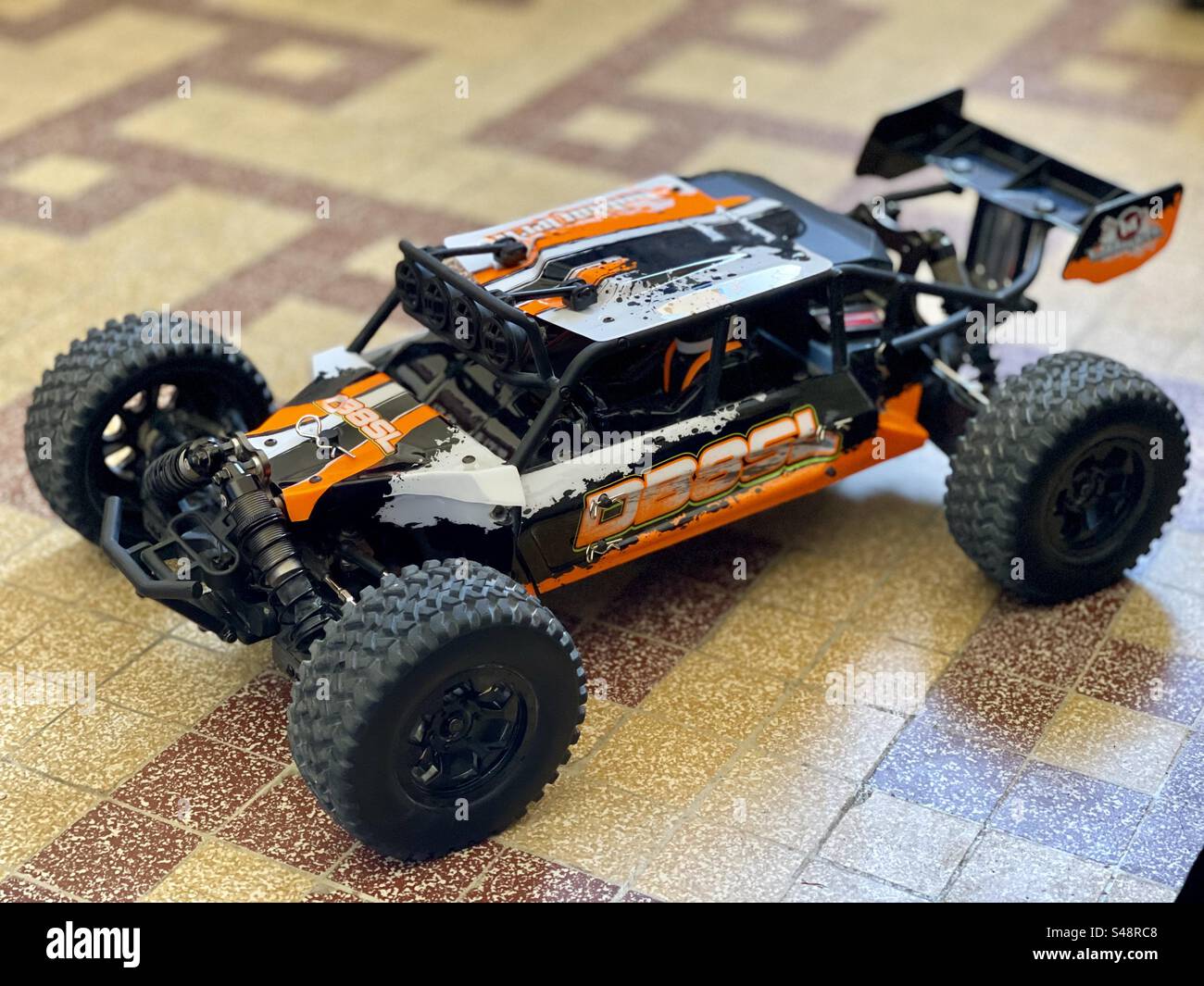 Shot of an orange, white and black splash DB8SL RC remote controlled model buggy on floor tiles - Smartphone Captured Stock Image