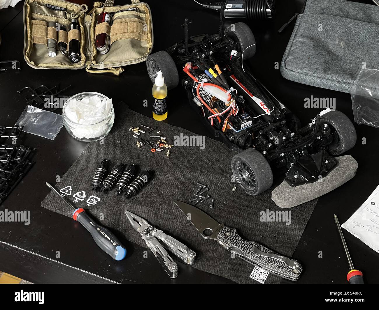 Shot of an RC work desk covered with precision screwdriver, pliers, a custom Spyderco knife, a set of shocks, a disassembled remote controlled race car, glue, oil, small screws and a set of tools - Smartphone Captured Stock Image