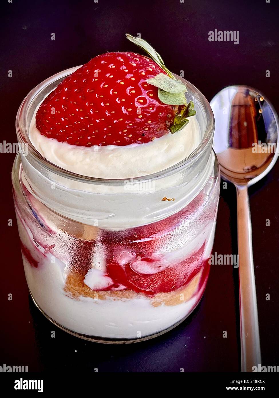 Shot of a Strawberry and cream reconstructed fraisier cake in a glass with a spoon in a French restaurant in France - Smartphone Captured Stock Image