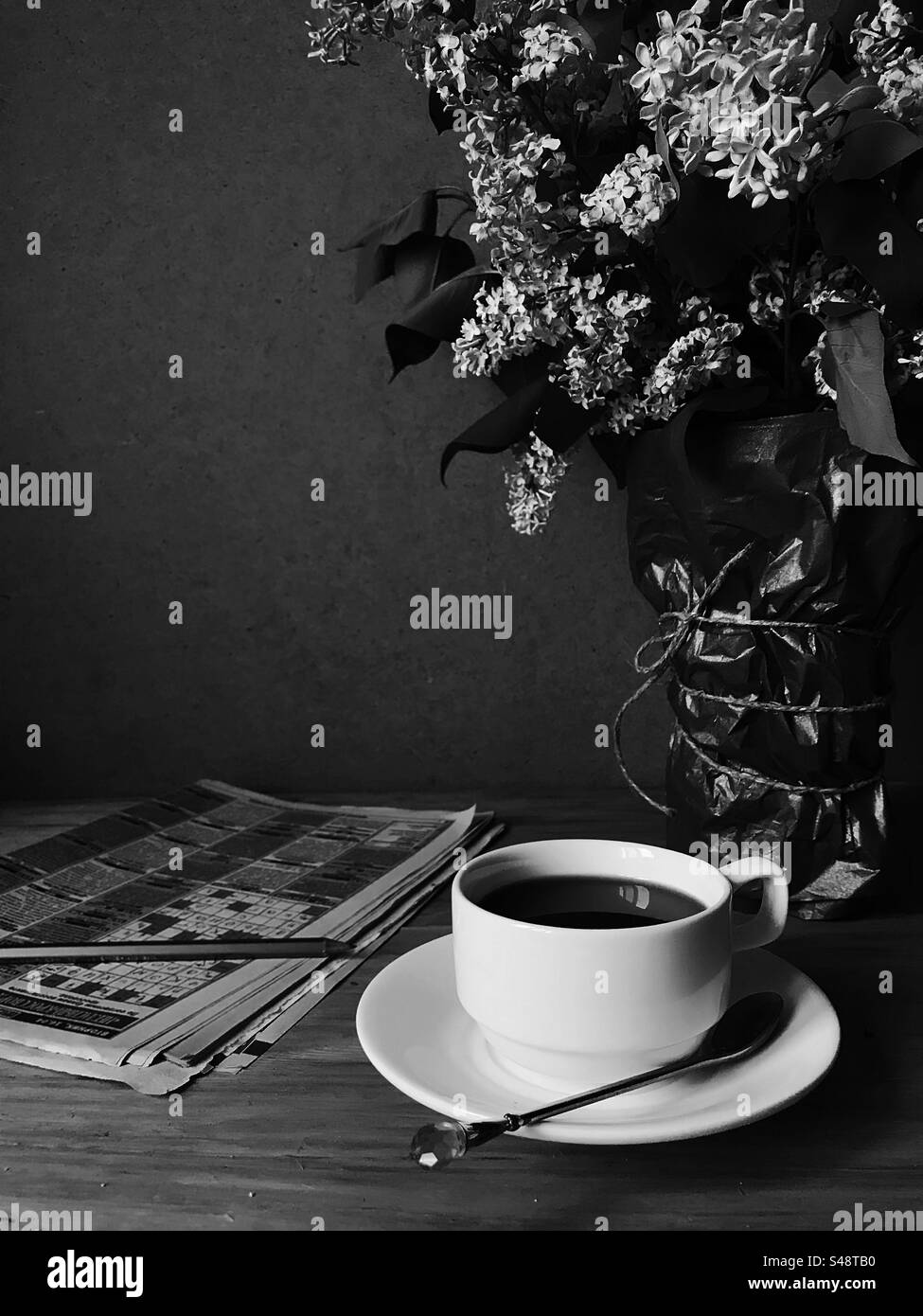 Coffee cup and crossword newspapers with lilac flowers in black and white - Smartphone Captured Stock Image
