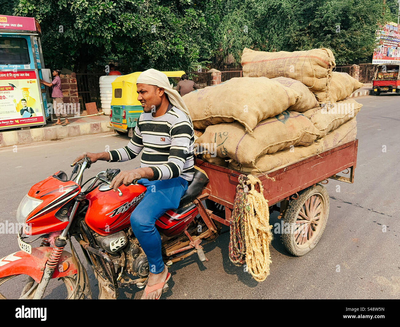 An indian man transporting vegetables in sacks to a market in India in a Jugad which is a modified motorcycle - Smartphone Captured Stock Image
