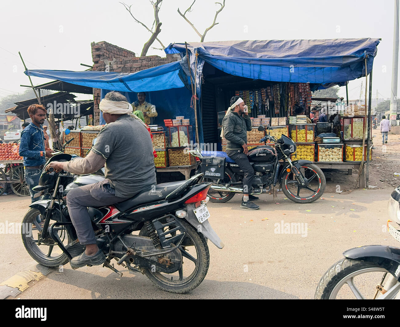 Motorbikes passing by shops selling Indian snacks in a small town in northern India - Smartphone Captured Stock Image