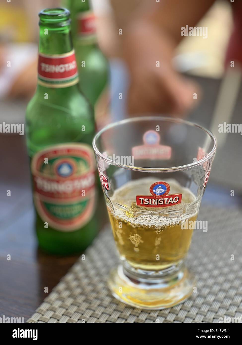 A glass of Tsing-Tao beer next to its empty bottle on a bar restaurant table in Palavas, Occitanie, France - Smartphone Captured Stock Image