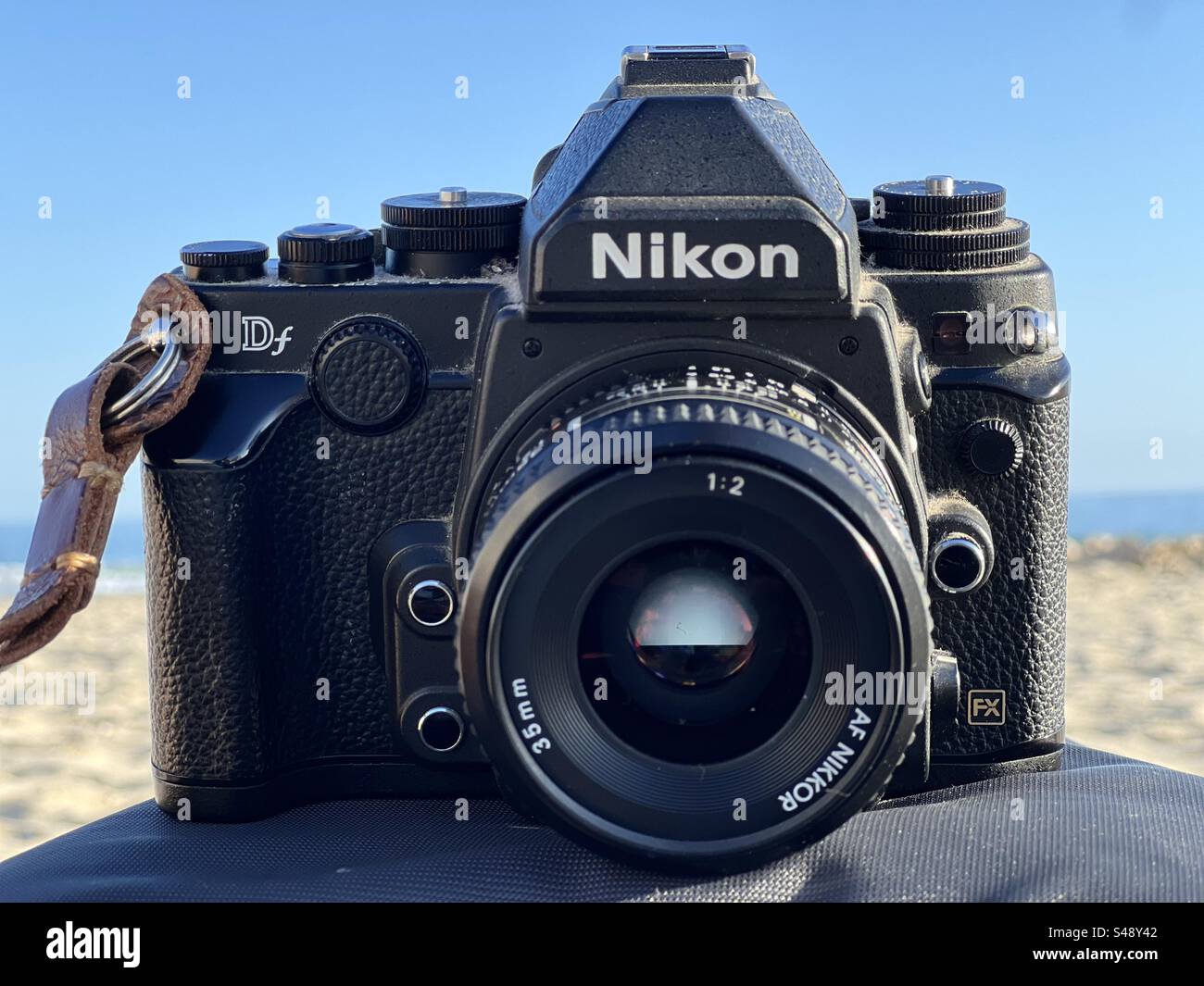 Front shot of a Nikon Df DSLR classic digital reflex camera on a car dashboard with background of breach. Stock Photo