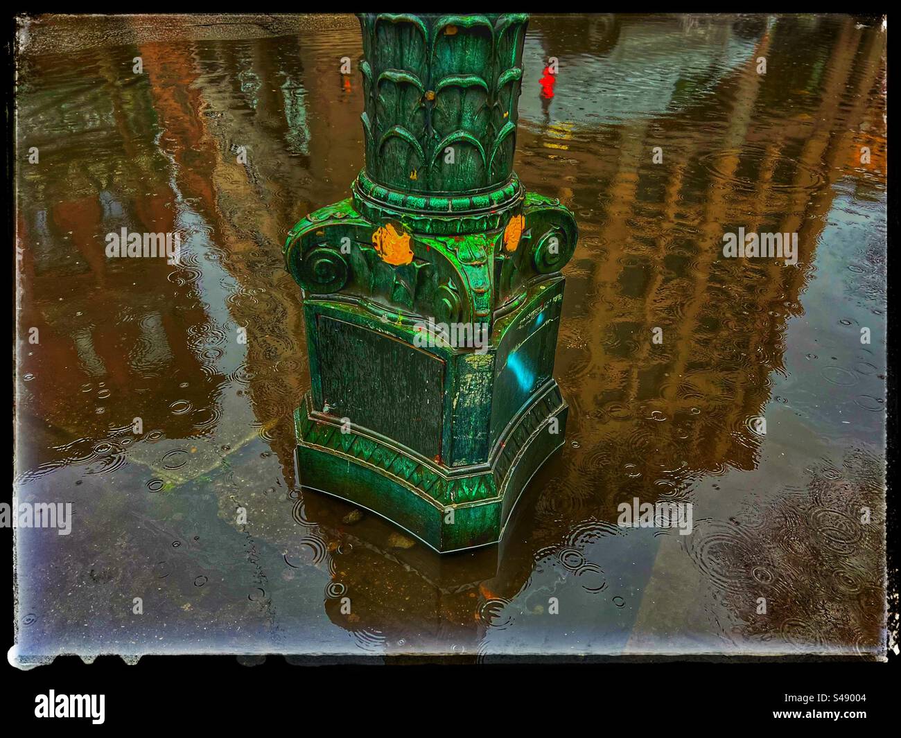 Flooded street after too much rain in Seattle covers part of sidewalk and base of old streetlight with reflections of buildings in the water puddle. - Smartphone Captured Stock Image