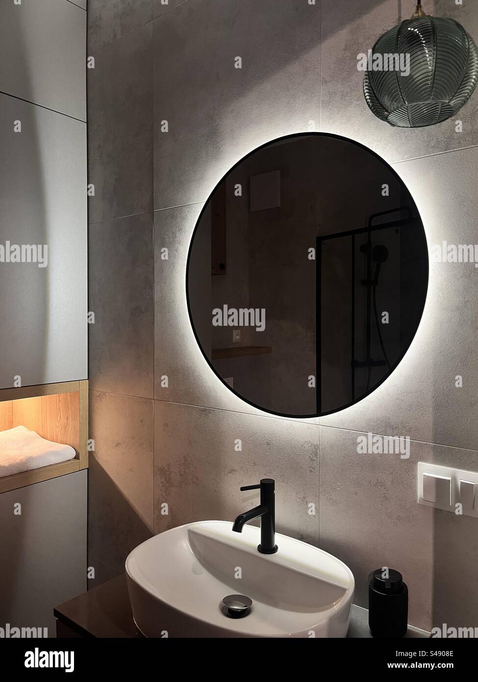 Modern home bathroom interior in low light with large backlit round mirror - Smartphone Captured Stock Image