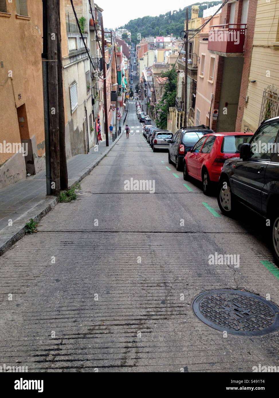 Narrow sloping city street with parked cars on one side in the old town of Barcelona, Catalonia, Spain - Smartphone Captured Stock Image