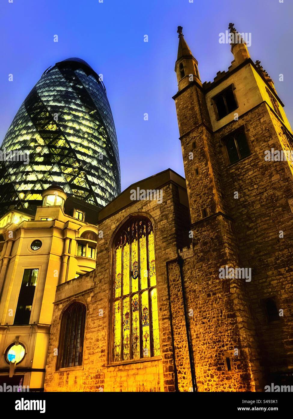 St Andrew Undershaft Church survived the Great Fire of London and the Blitz. Shown with illuminated stained glass windows and the modern Gherkin building in the City of London - Smartphone Captured Stock Image