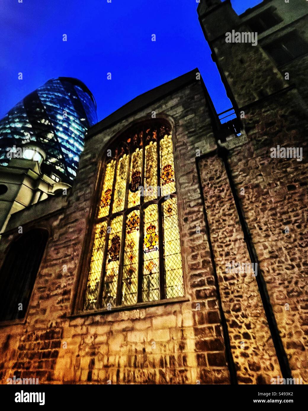 Backlit stained glass window of St Andrew Undershaft Church in the City of London. Night photography. The modern architecture of the City includes the Gherkin - Smartphone Captured Stock Image