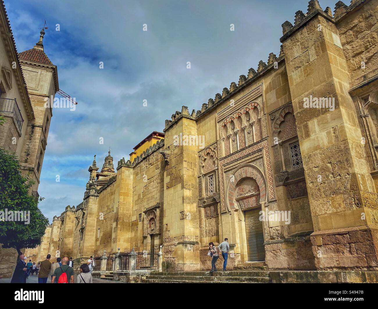 People walk around beautifully decorated external walls of Mosque-Cathedral in Córdoba, Spain. - Smartphone Captured Stock Image
