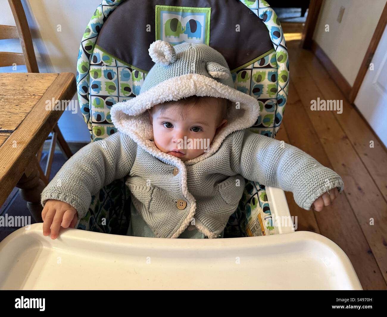 Baby girl bundled up waiting and sitting in a high chair. - Smartphone Captured Stock Image