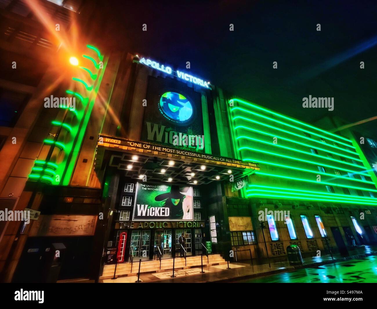 Landscape photograph of the Apollo Theatre in Victoria, London seen at night with green neon lighting advertising “Wicked” a long running musical based on the wizard of Oz. Nightlife in the streets. - Smartphone Captured Stock Image