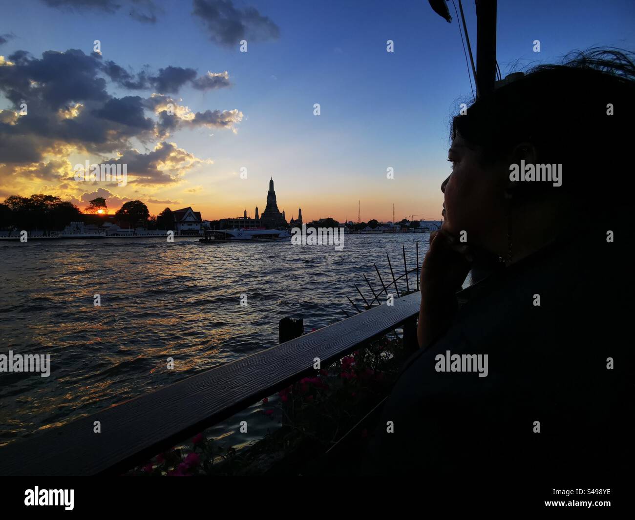 A traveler enjoying a beautiful sunset over the Chao Phraya river and Wat Arun in Bangkok. - Smartphone Captured Stock Image