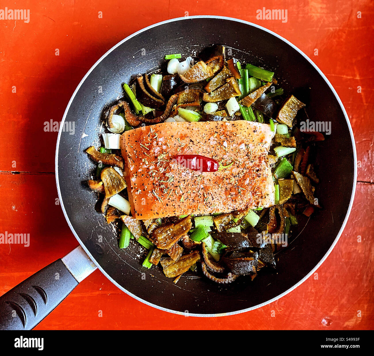 Salmon fish filet surrounded by onion and green chile poblano chilli peppers with a red hot chilli pepper on top in Queretaro, Mexico - Smartphone Captured Stock Image