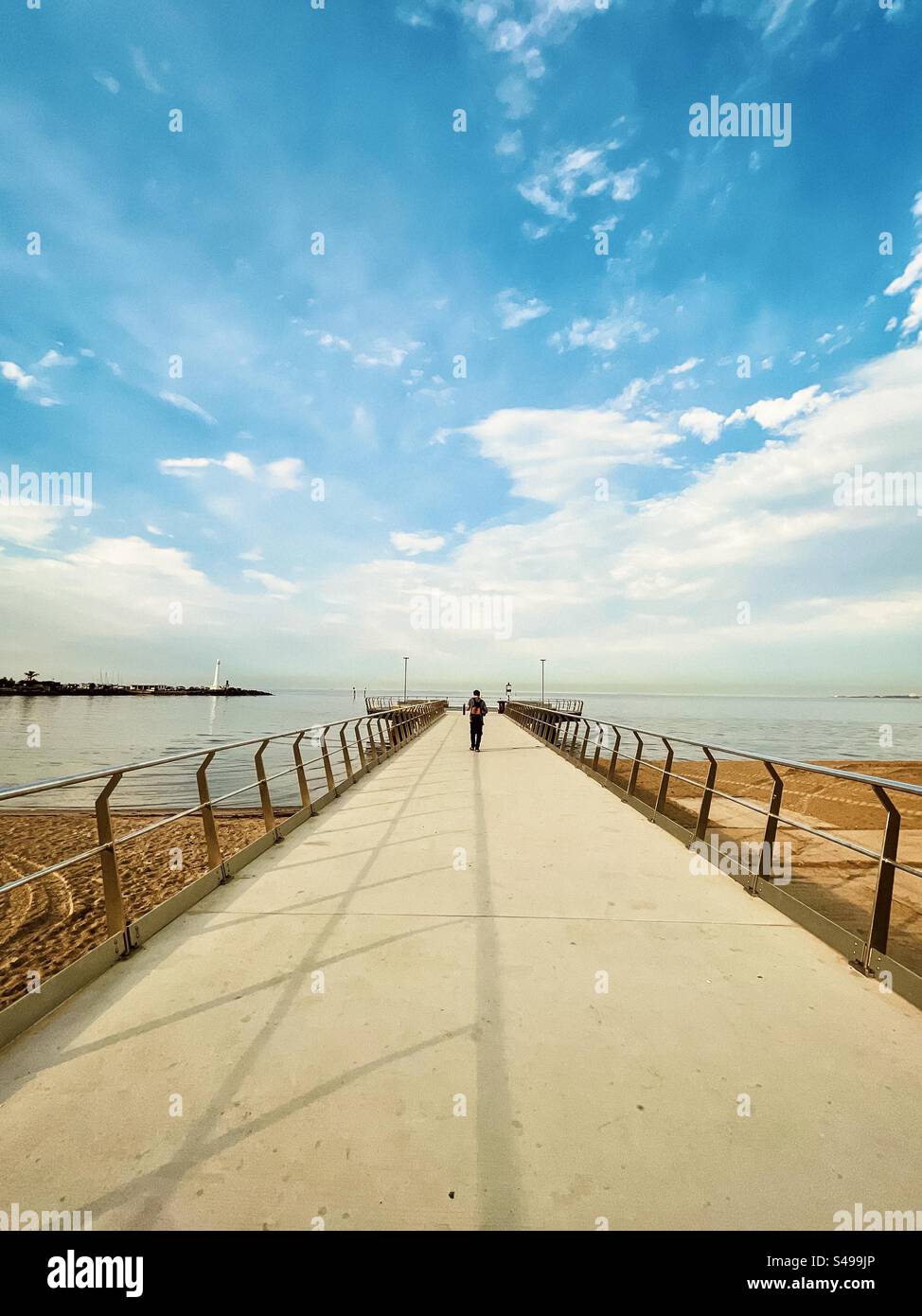 Rear view of a man walking on the pier towards the Shakespeare Grove viewing platform in the sea in St. Kilda, Victoria, Australia. Solitude. The way forward. Diminishing perspective. Scenics-nature. - Smartphone Captured Stock Image