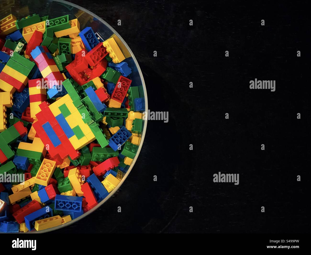 Directly above view of glass bowl filled with colorful Lego bricks on black wooden table with copy space. - Smartphone Captured Stock Image