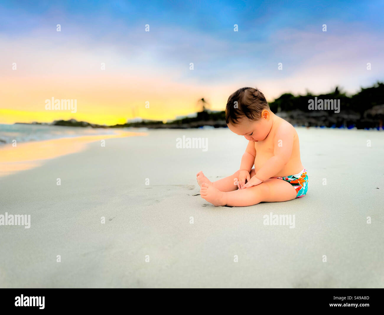 Beach trip with baby. Baby sitting on the sand with face looking down exploring with her hands. Varadero, Cuba - Smartphone Captured Stock Image