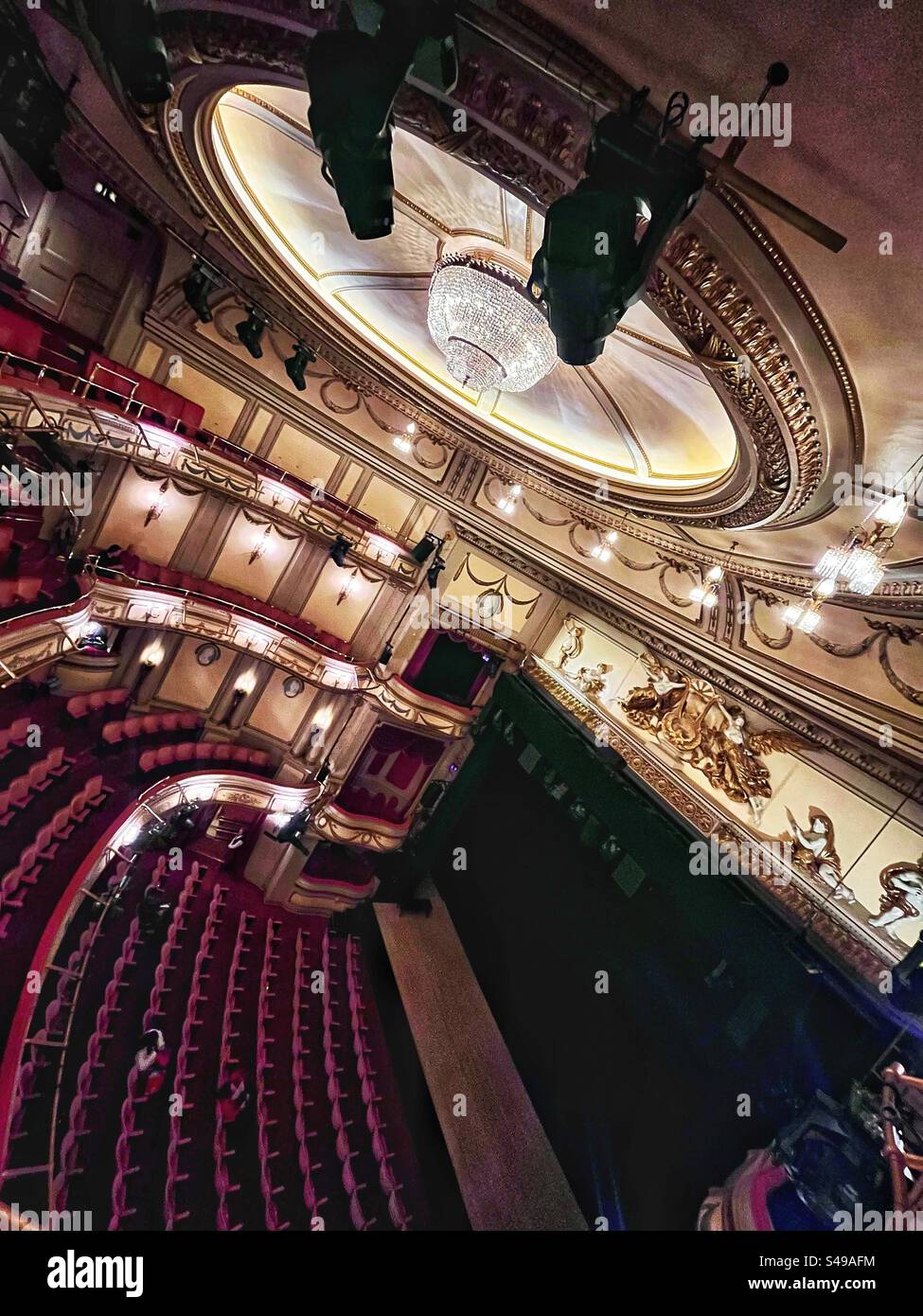 The grandiosity of the rococo interior of The Noel Coward Theatre in London. Lights are up and stage curtains closed. Stalls with a person waiting. Perspective from the balcony. - Smartphone Captured Stock Image