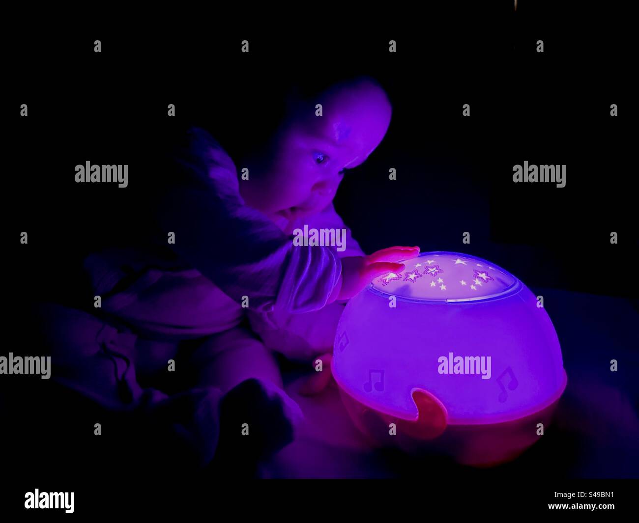 Baby amazed at night lamp that displays star shapes before bedtime Stock Photo