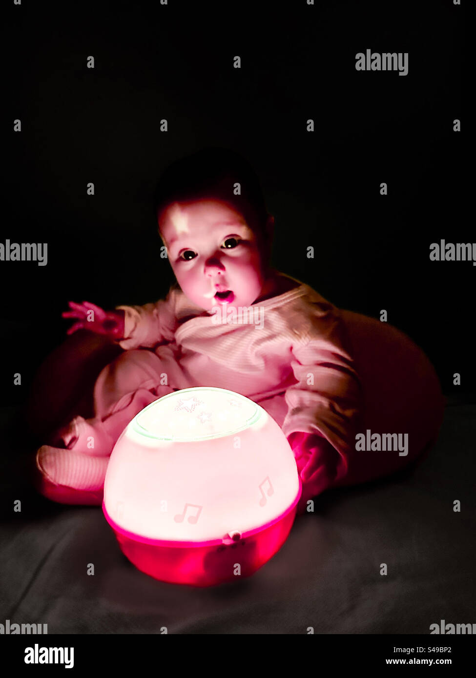 Baby amazed at night lamp that displays star shapes before bedtime Stock Photo